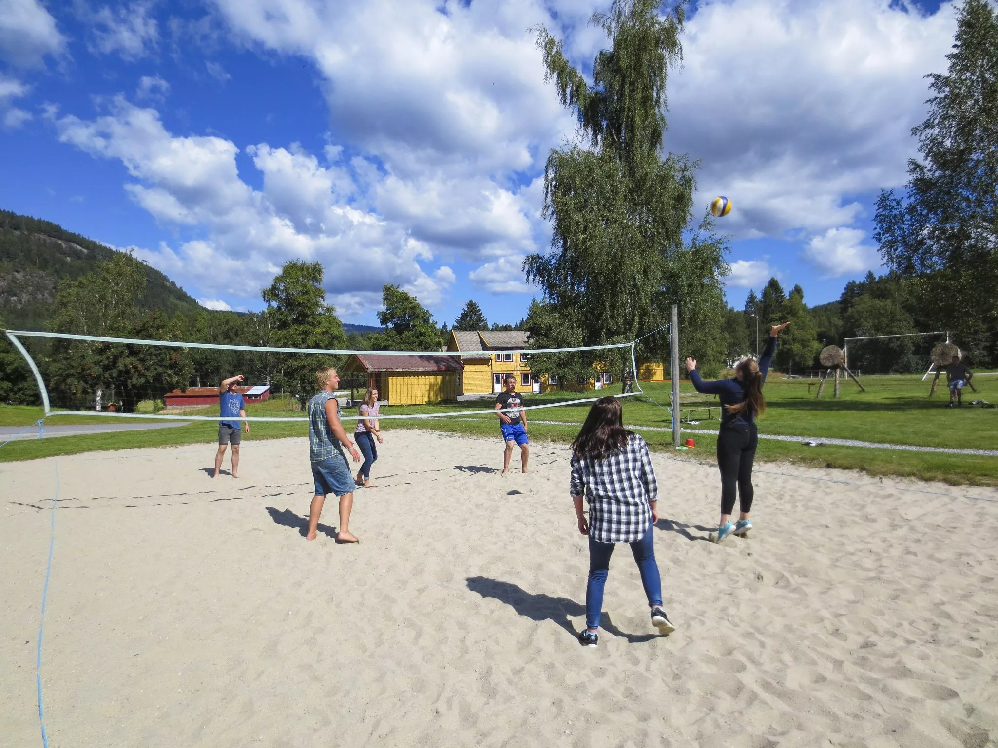 Elever spiller sandvolleyball med de gule skolebyggene i bakgrunnen