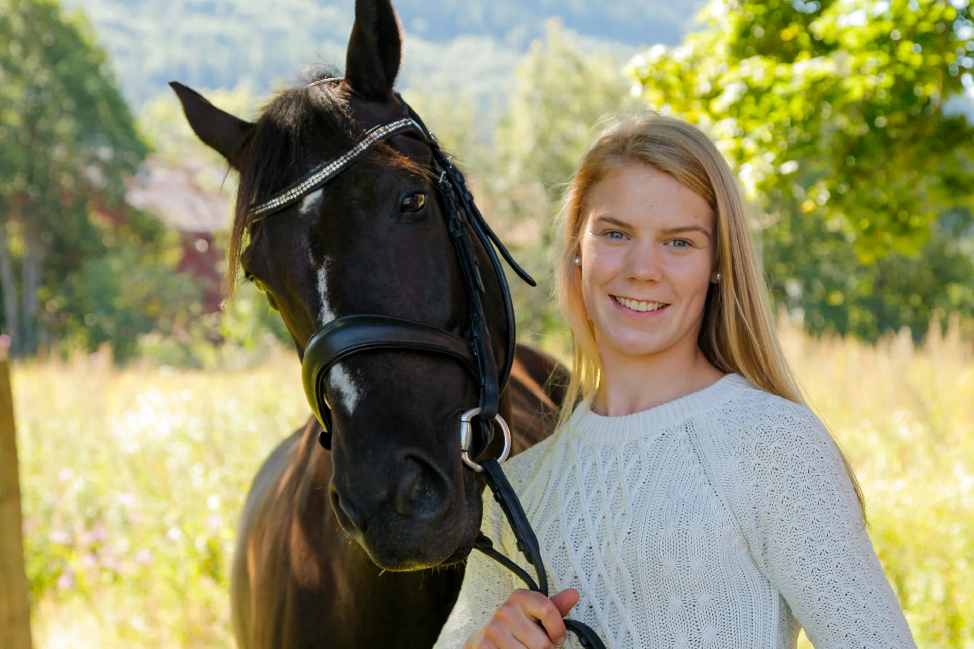 Smilende elev med en svart hest i sommerlys