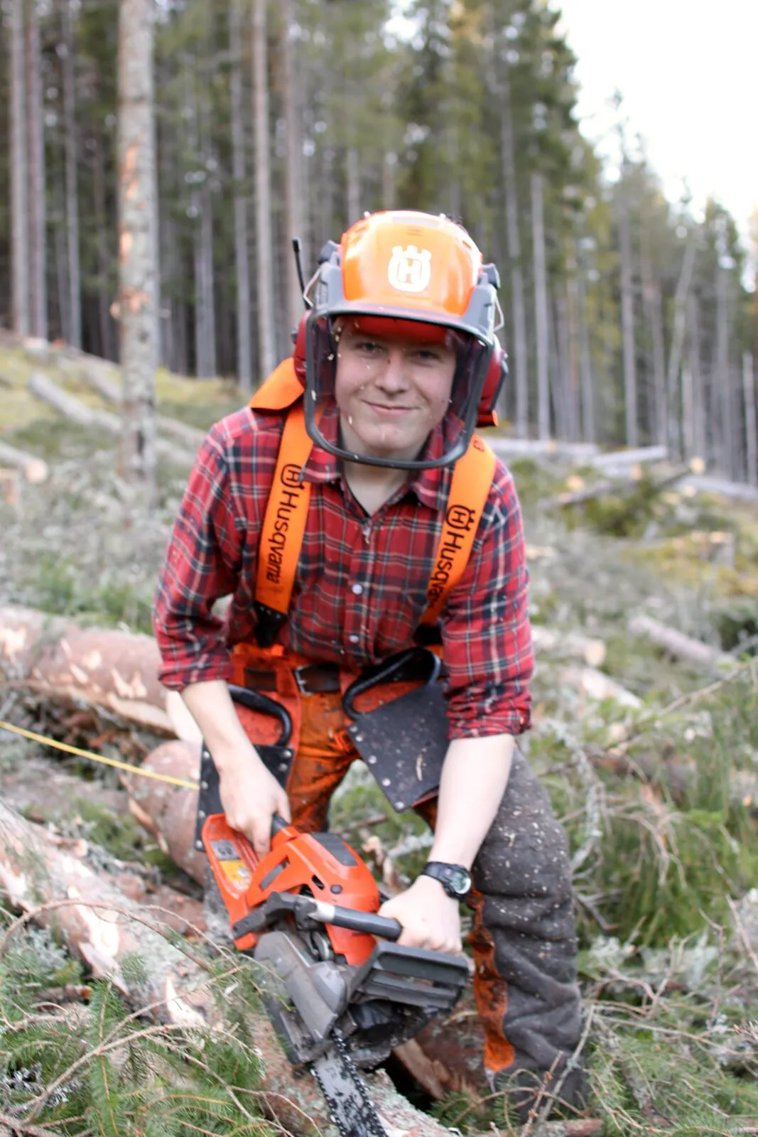 Elev i hjelm og verneklær med motorsag på hogstfelt